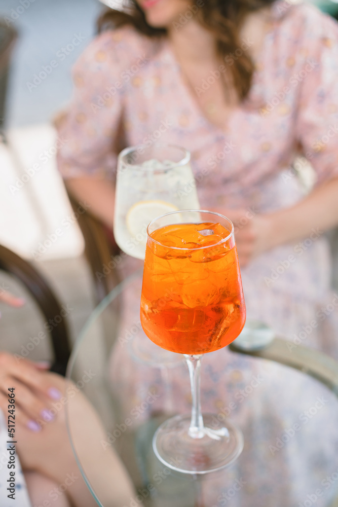 Fototapeta premium Summer aperol cocktail on table. Friends having drinks in cafe together. Lifestyle concept. Outdoors.