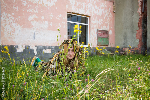 a young girl lies in the grass in a camouflage military costume near the old wall of an abandoned building photo