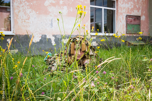 a young girl lies in the grass in a camouflage military costume near the old wall of an abandoned building photo