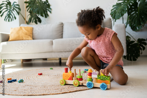 Black lovely toddler in pink t shirt playing with a wooden train. Little girl play with wooden train at home. Happy small child feel playful rest enjoy leisure weekend