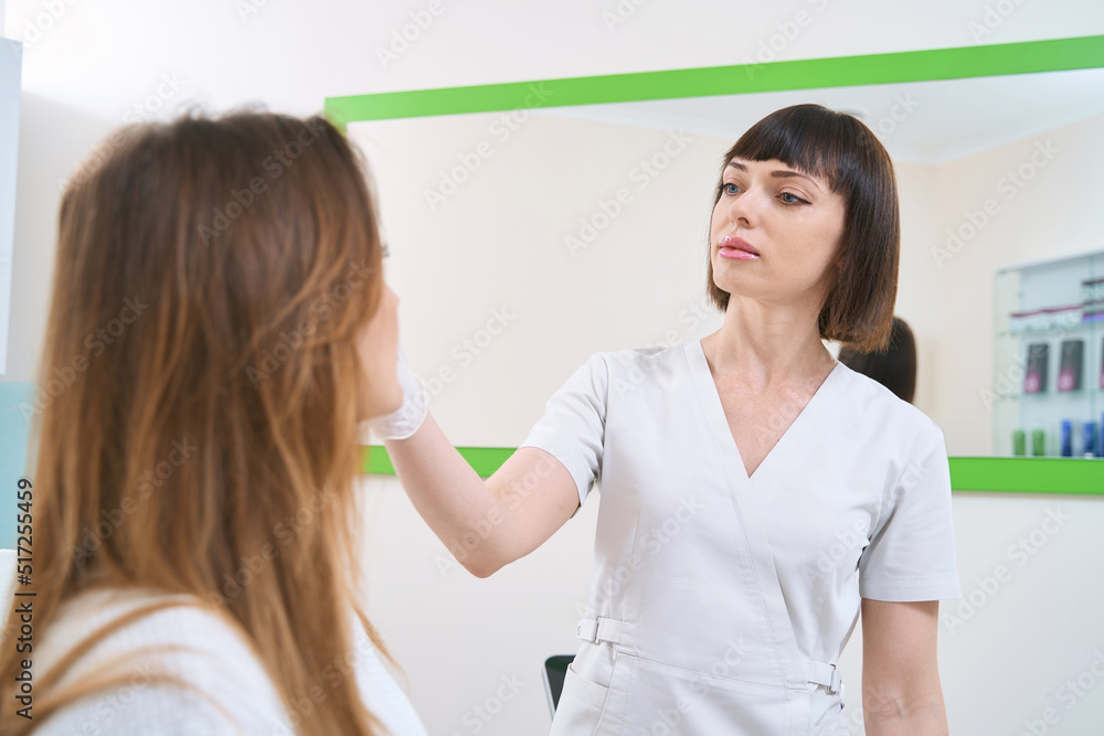 Doctor examining skin of female face in cosmetology center Doctor examining skin of female face in cosmetology center