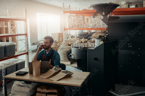 Business owner of small coffee roasting factory talking phone on his workplace