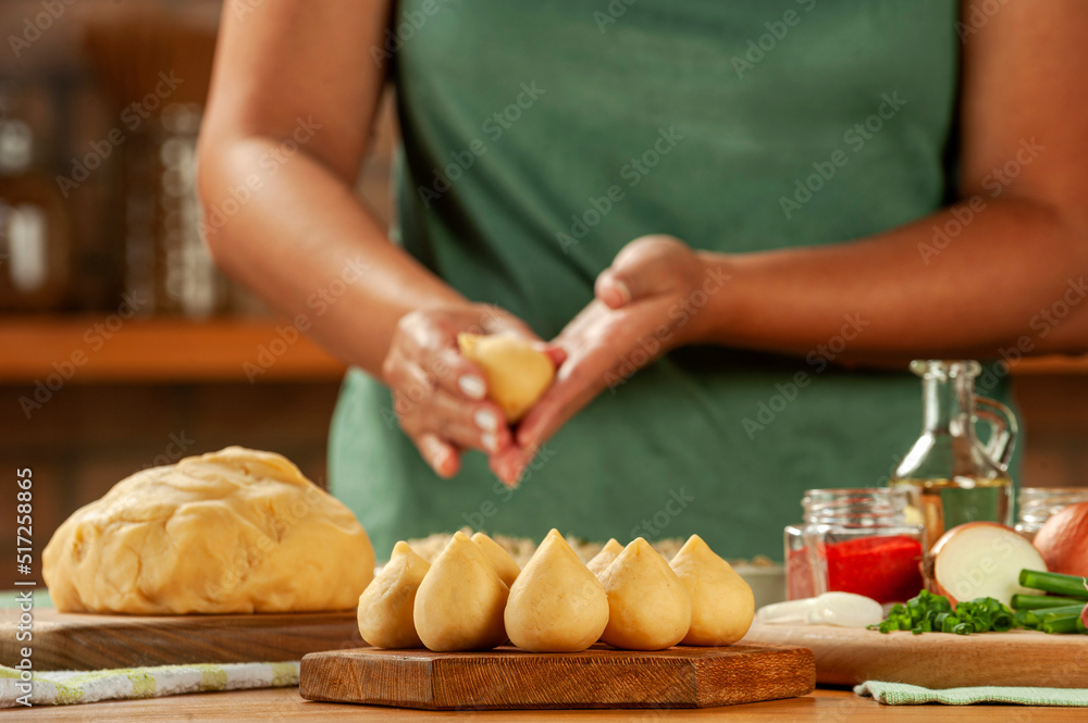 Woman hands preparing brazilian croquette (coxinha de frango) on a wooden table. Woman hands preparing brazilian croquette (coxinha de frango) on a wooden table.