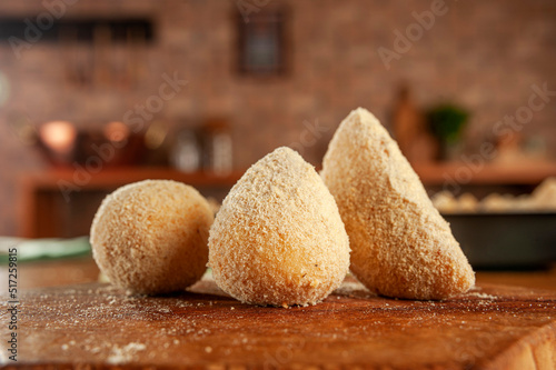 Breading brazilian croquettes (coxinha de frango, risolis de carne e bolinha de queijo) on kitchen bricks wall background. photo