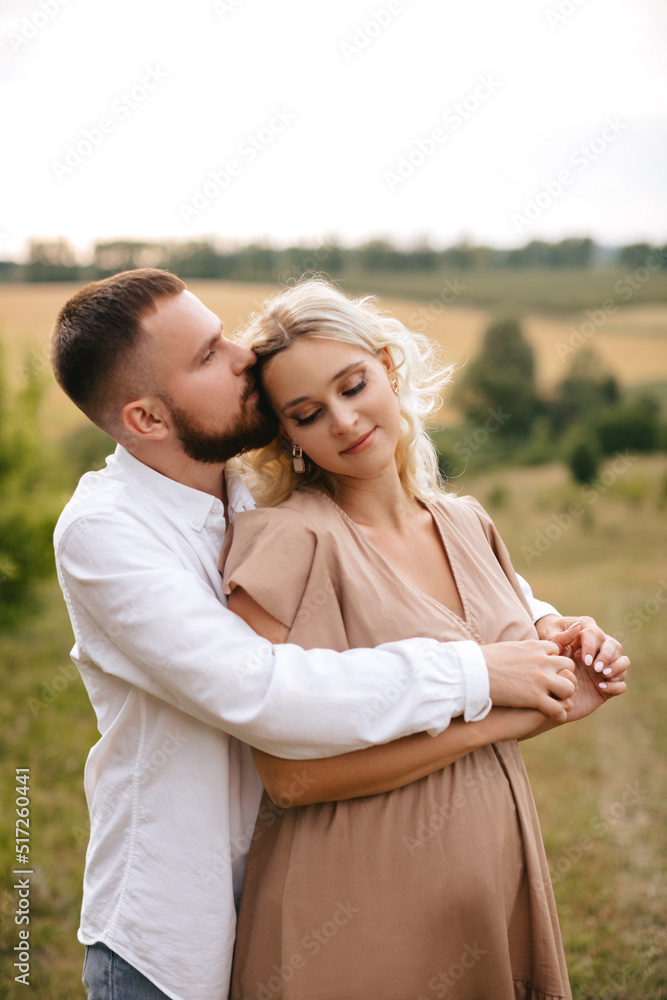 Fototapeta premium Loving man hugging his pregnant wife from behind in nature.