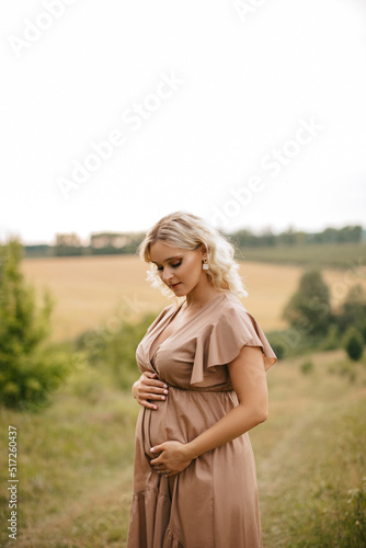 A pregnant woman in a dress touches her belly in a wheat field at sunset. The pregnancy concept. 