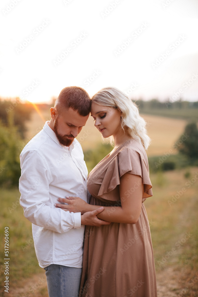 A man with beard is holding hands with his pregnant wife in a field at sunset. A man with beard is holding hands with his pregnant wife in a field at sunset.