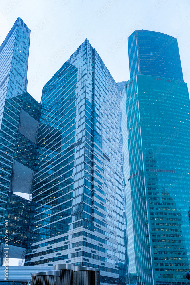 The tops of modern corporate buildings in snowfall. Low angle view of skyscrapers.