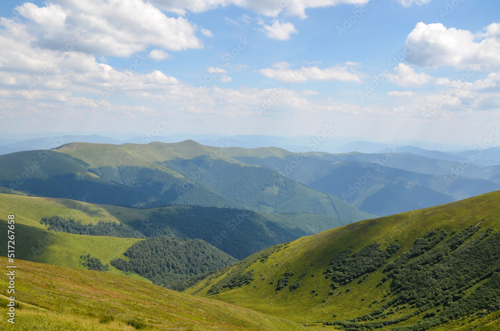 The landscape of the mountains. Beautiful mountain ranges with green hills and forest under blue sky on summer day. Carpathians, Ukraine