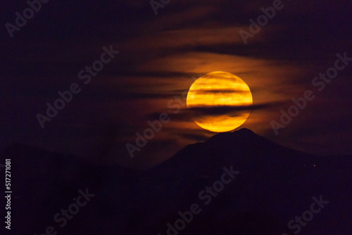Obraz na plátně Large Harvest moon rising over Arizona mountains, partially covered by clouds