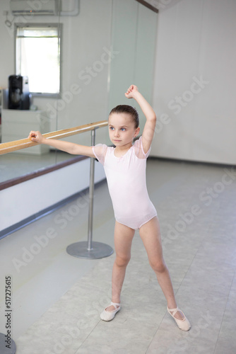 Cute little girl toddler ballerina in pale pink tutu and ballet shoes practicing dance moves.