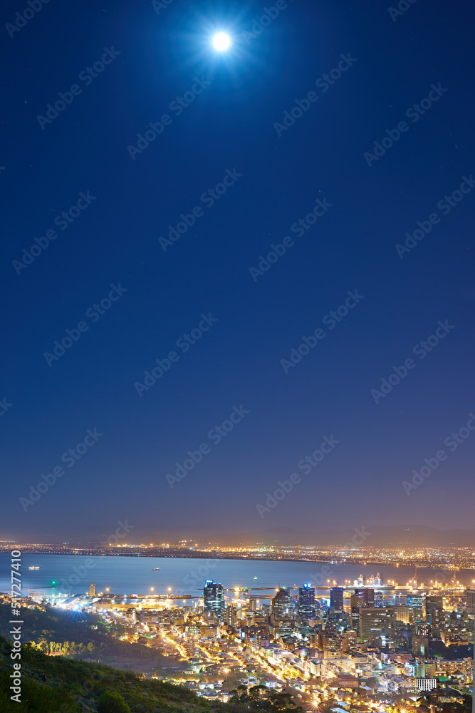 Urban city lights with a full moon in the midnight sky with copy space. Skyline with colorful lighting with the wide open ocean on the horizon. City buildings at night in Signal Hill, South Africa