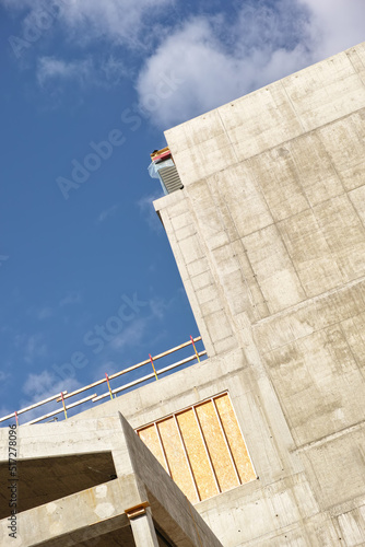 Exterior of a concrete building against a cloudy blue sky. Detail view of a tall residential or office building made of exposed concrete slabs. Construction phase of home remodel and addition