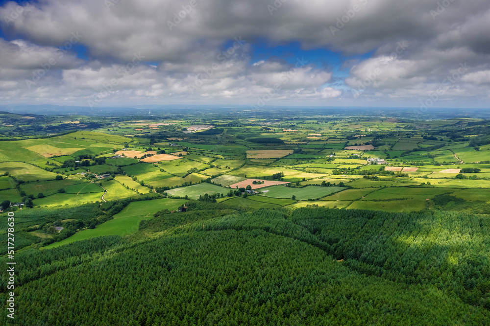 Aerial view on hills with green grass fields and forests in county Tipperary, Ireland. Emerald island nature. Irish landscape. Blue cloudy sky. Devils bit area.