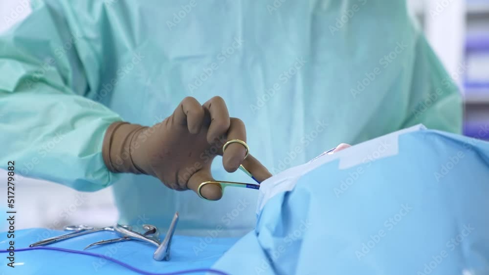 Gloved hands of unrecognized surgeon using metal instrument sewing the patient at the end of operation. Close up. Gloved hands of unrecognized surgeon using metal instrument sewing the patient at the end of operation. Close up.