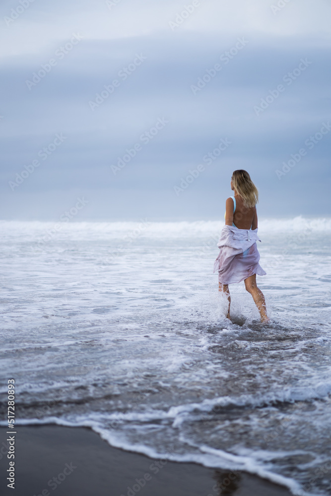 A young woman walks along the ocean at dawn, a time of meditation and reflection.