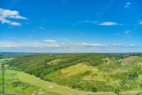 An agricultural landscape with green pasture and hill in summer. Aerial view of a farm with lush grass against a cloudy blue sky with copyspace. Peaceful farmland with calming  soothing scenic views