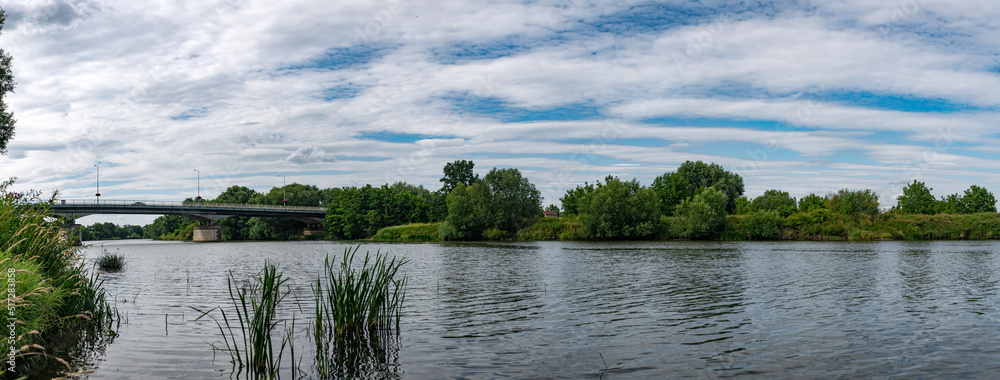 krajobraz rzeki Odry w zachodniej Polsce w jasnych zielono niebieskich barwach i lekko pochmurnej pogodzie - obrazy, fototapety, plakaty 