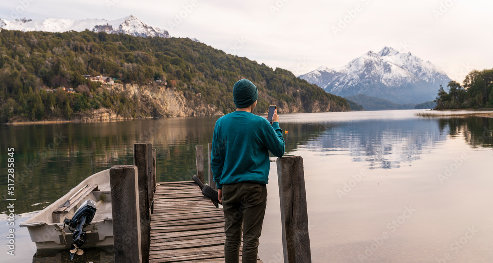 Joven turista sacando fotos con su celular y enviándole  a sus amigos durante un paseo por la Patagonia Argentina, Bariloche, Sudamerica. 