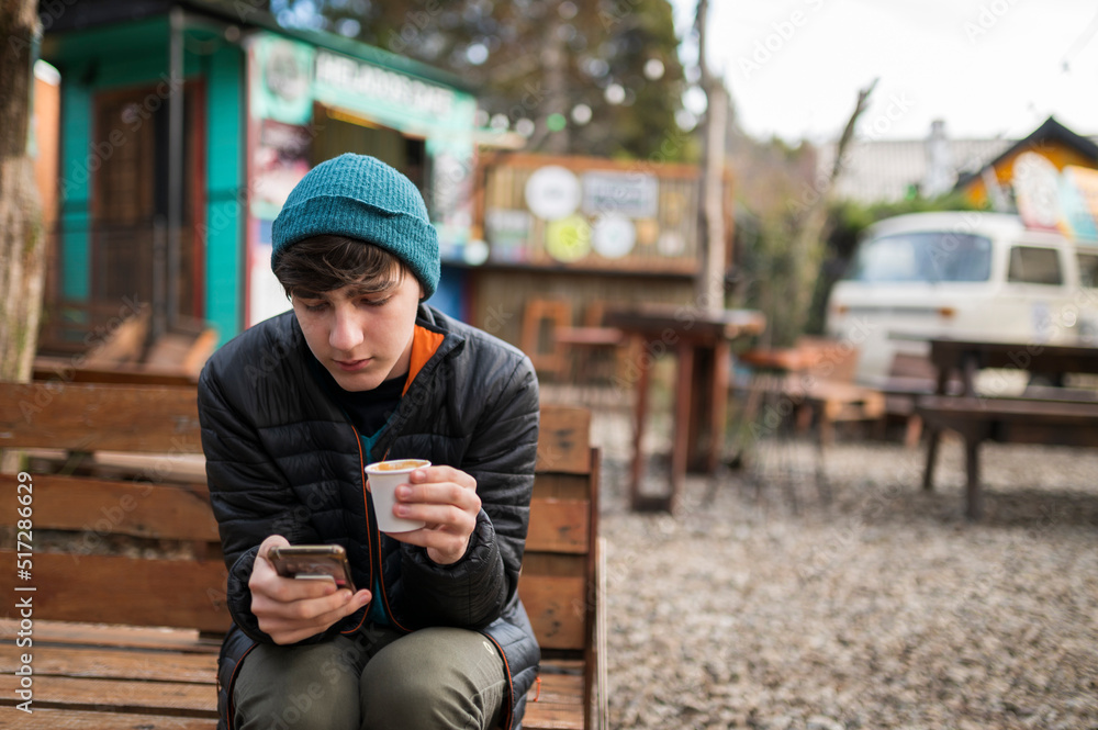 Joven disfrutando un rico café mientras observa su teléfono celular en un paraje de comidas rápidas. Joven disfrutando un rico café mientras observa su teléfono celular en un paraje de comidas rápidas.
