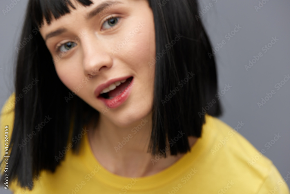 a close horizontal photo of a beautiful, pleasant woman with short straight, black hair smiling pleasantly looking into the camera while standing in a yellow T-shirt on a gray background a close horizontal photo of a beautiful, pleasant woman with short straight, black hair smiling pleasantly looking into the camera while standing in a yellow T-shirt on a gray background