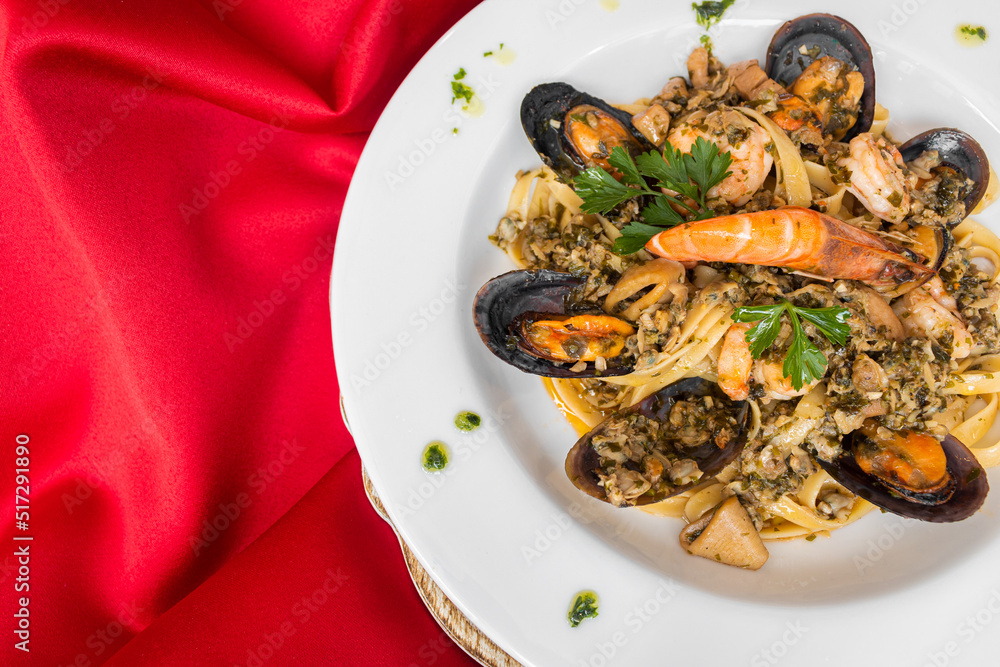 Pasta macarrão italiano em prato branco com fundo vermelho com camarão, lagosta, ostras, bonito, com molho de tomate, com flor de tomate