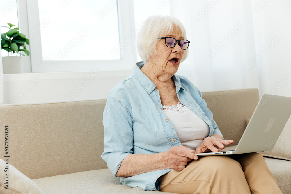 an elderly woman is sitting in a stylish shirt with a laptop on her lap and looks at the monitor with her mouth wide open in surprise, communicating via video link, keeping in touch with loved ones an elderly woman is sitting in a stylish shirt with a laptop on her lap and looks at the monitor with her mouth wide open in surprise, communicating via video link, keeping in touch with loved ones