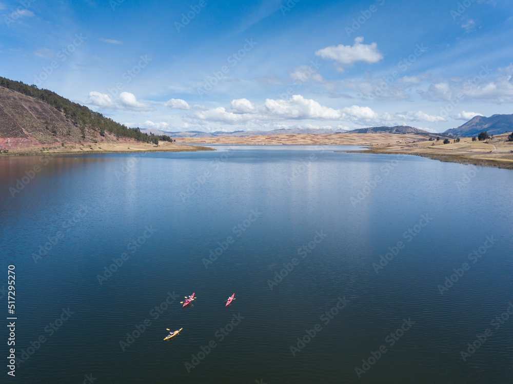 Aerial view of people sailing in Huaypo Lake. Water source in the high Andes of Cusco Peru. Sunny day in Andean rural landscape. Open air sport with kayaks. 