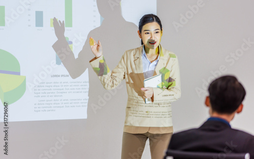 Unrecognizable unknown businesswoman audience in formal suit sitting in conference meeting room holding hand up asking question while Asian female presenter presenting graph chart data on wall screen