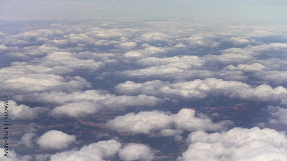 Airplane over white puffy clouds in earth surface. Window view of the wing of an airplane Airplane over white puffy clouds in earth surface. Window view of the wing of an airplane