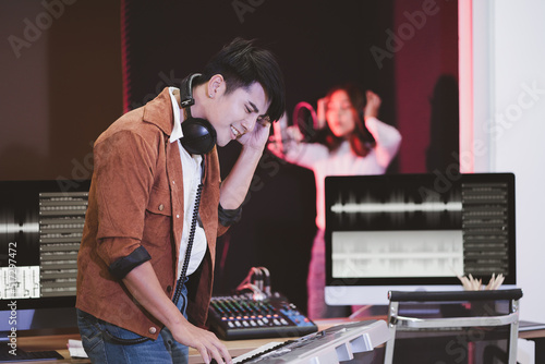 Asian producer standing by sound mixing console. Happy male music composer artist with a woman singer background