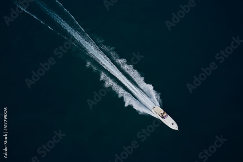 Fast moving white boat with people aerial view. Super speed white boat fast movement on dark water top view. © Berg