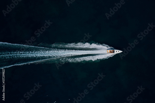 Super speed white boat fast movement on dark water top view. Fast moving white boat with people aerial view. © Berg