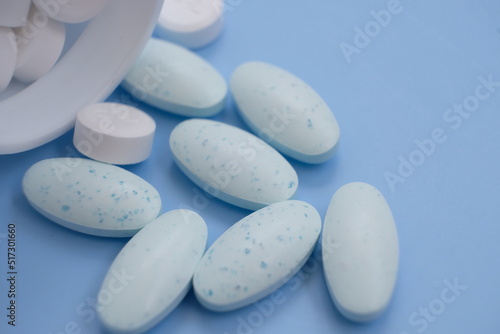 Pharmaceutical medical pills, blister-packaged capsules, and tablets strewn across a blue background.