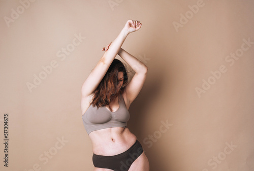 Foto Young attractive woman plus size in underwear dancing on beige background, body