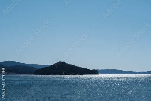 A small sailboat crosses in front of the island of Tambo, in the Ria de Pontevedra, in Galicia (Spain) photo