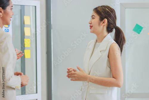Closeup shot of millennial Asian happy cheerful pretty businesswoman employee standing smiling greeting talking discussing with unrecognizable unknown female colleague in company office meeting room