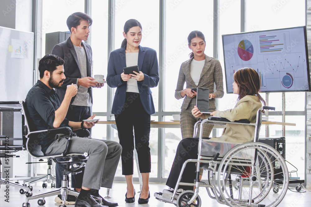 Group of millennial multinational multicultural Asian Indian businessmen and businesswomen with disabled handicapped partner sitting on wheelchair taking coffee break discussing together in office Group of millennial multinational multicultural Asian Indian businessmen and businesswomen with disabled handicapped partner sitting on wheelchair taking coffee break discussing together in office