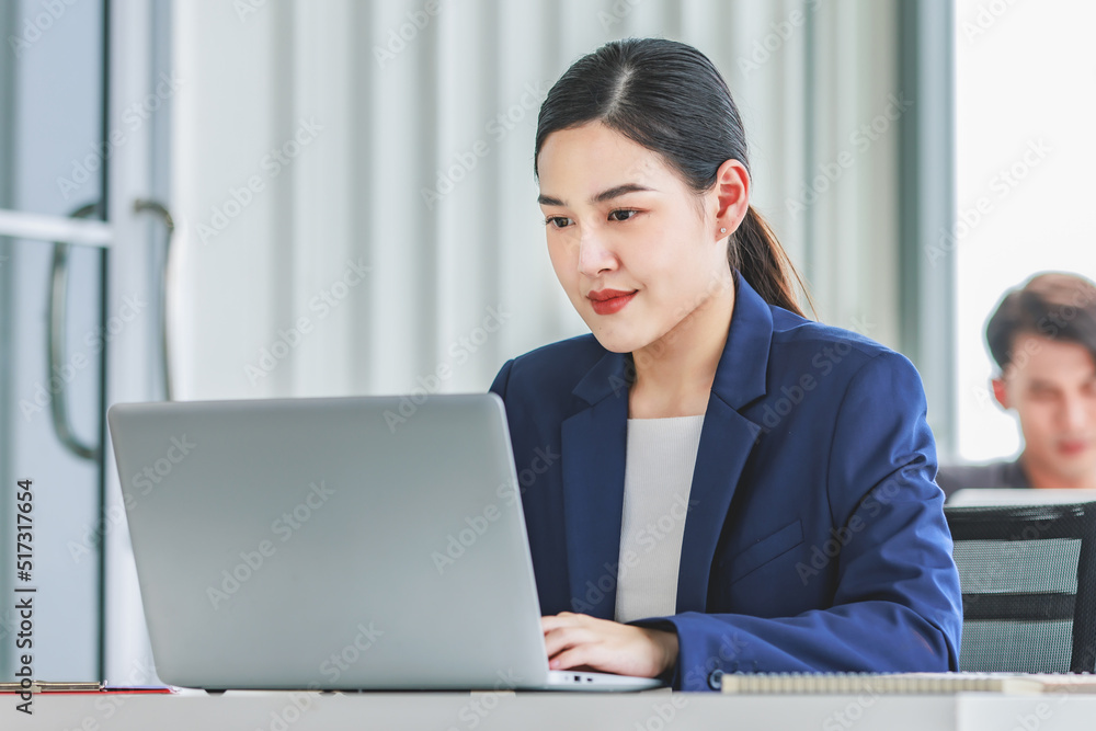 Closeup shot of millennial Asian young beautiful smart professional female businesswoman employee in formal suit sitting working on workstation desk typing laptop notebook computer in company office Closeup shot of millennial Asian young beautiful smart professional female businesswoman employee in formal suit sitting working on workstation desk typing laptop notebook computer in company office