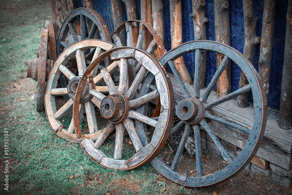 antique wooden cart wheels stand on the street on the lawn near the old barn on the territory of the household in the village in the private sector on the farm