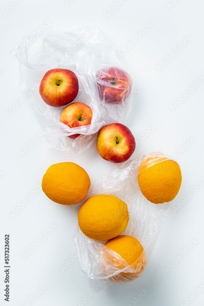 Fresh ripe oranges, apples in transparent plastic bags on a white background. Top view, flat lay Fresh ripe oranges, apples in transparent plastic bags on a white background. Top view, flat lay