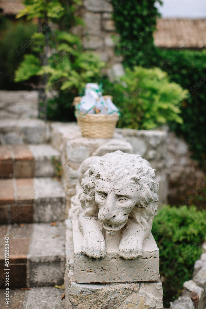 Old stone sculpture of a lion on the stone railing of the stairs. In the background is a stone facade entwined with green wisteria.