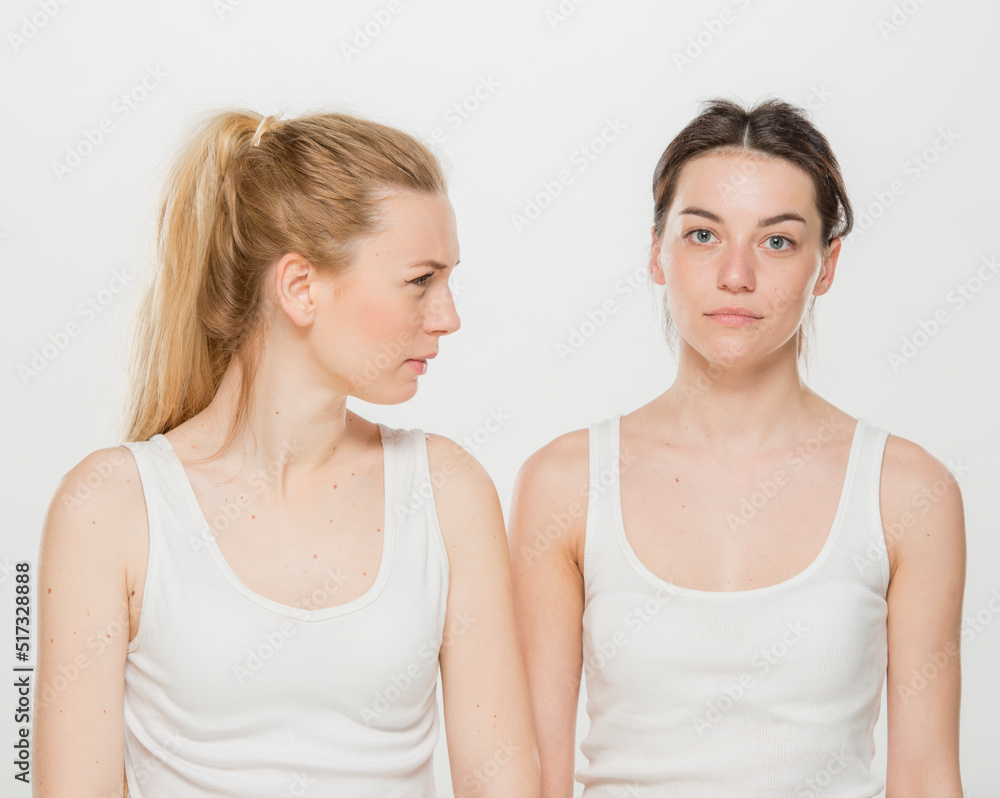 the girl tells the news to her friend. portrait of two girls in white t-shirts on a white background isolated. the girl tells the news to her friend. portrait of two girls in white t-shirts on a white background isolated.