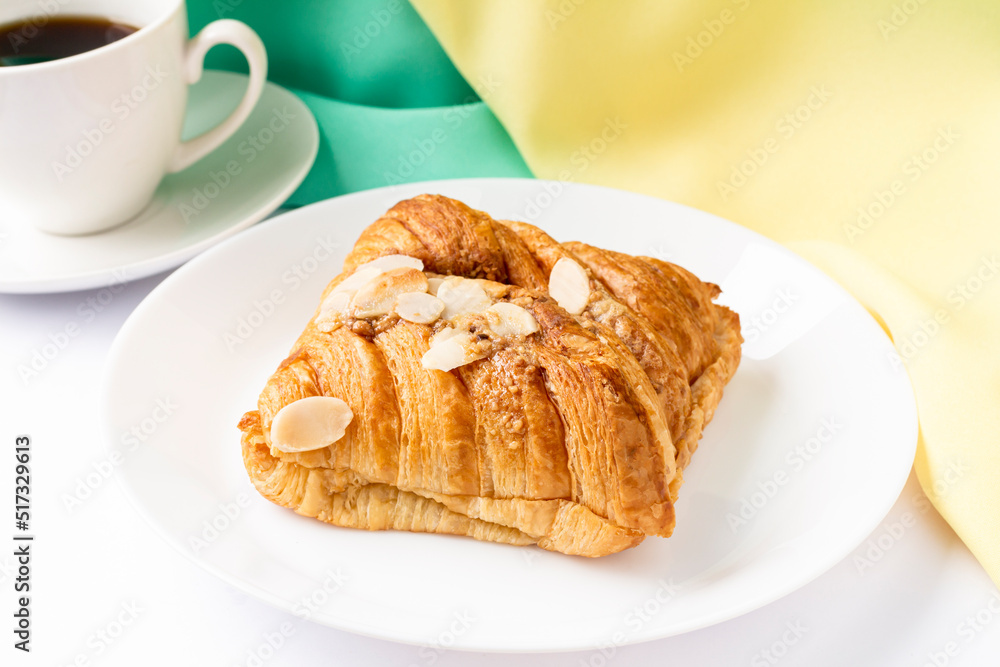 Almond croissant for breakfast on white plate with yellow green background, flat lay, top view. Almond croissant for breakfast on white plate with yellow green background, flat lay, top view.