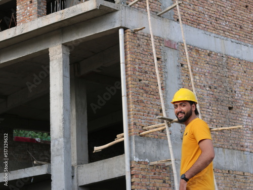 Young engineer wearing yellow safety helmet looking at blueprints in house at construction site © Muhammad
