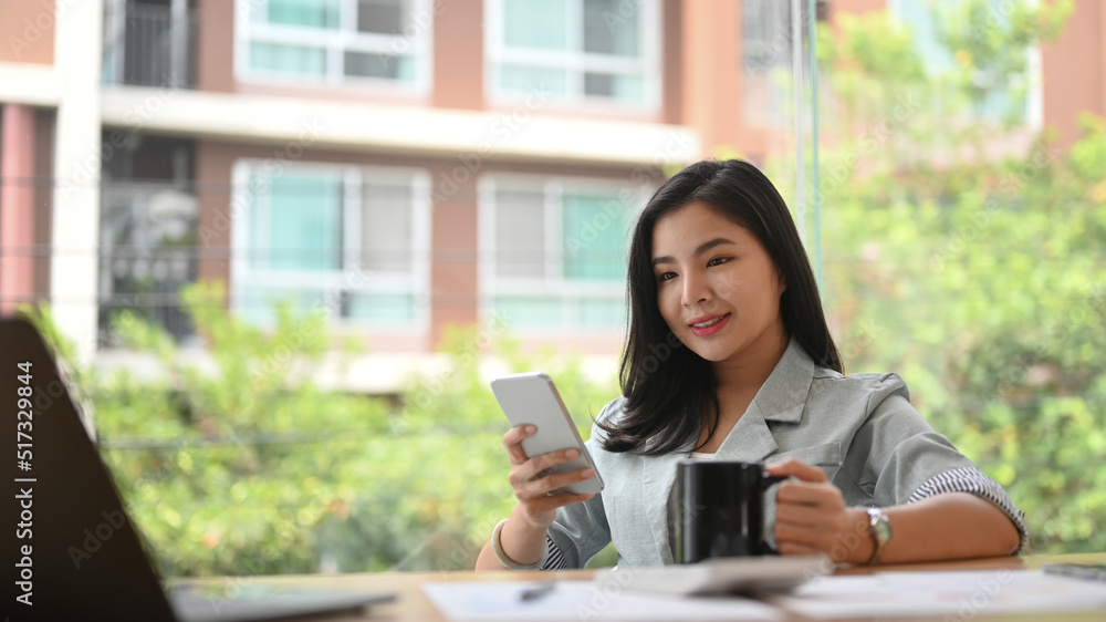 Pretty asian employee using mobile phone during taking coffee break at modern office Pretty asian employee using mobile phone during taking coffee break at modern office
