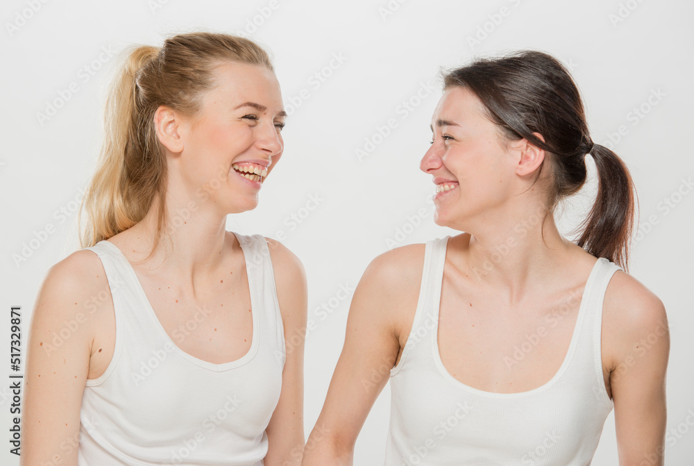 two girls are laughing.close-up portrait of two girls in white t-shirts on a white background isolated. two young Ukrainian girls, a brunette and a blonde, laugh merrily. two girls are laughing.close-up portrait of two girls in white t-shirts on a white background isolated. two young Ukrainian girls, a brunette and a blonde, laugh merrily.