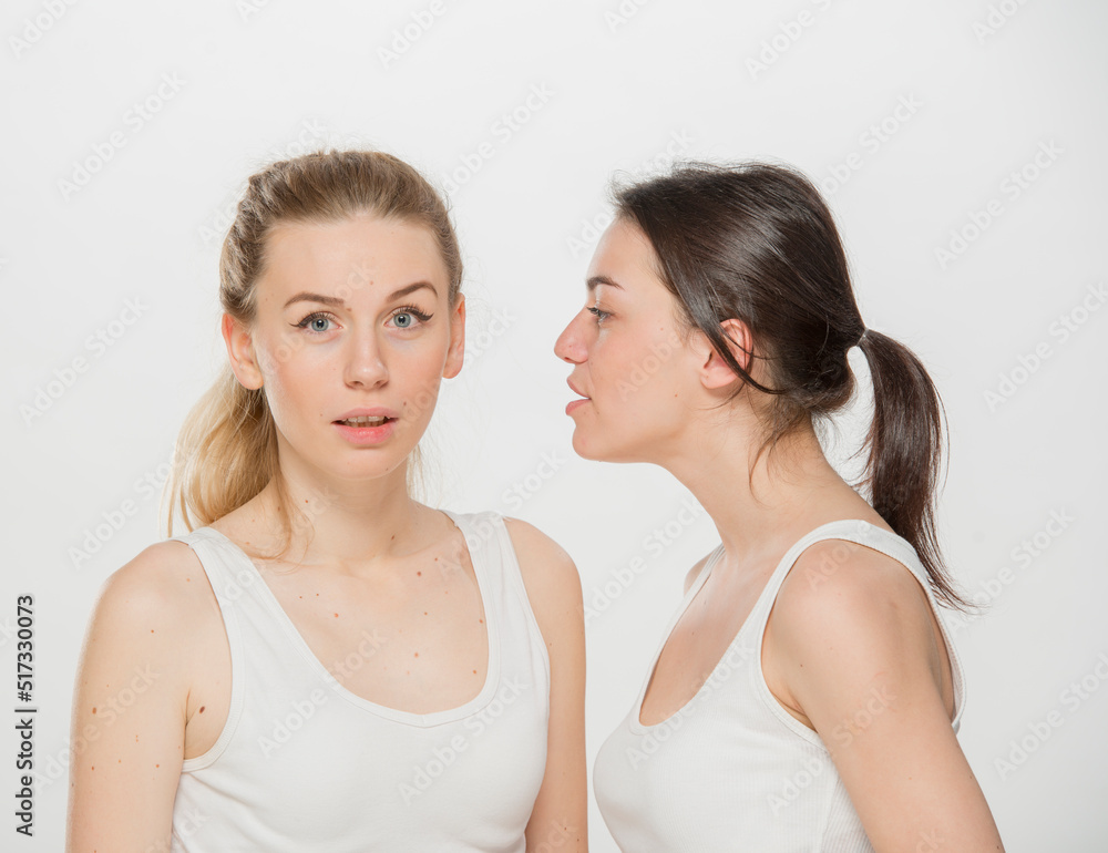 the girl tells the news to her friend. portrait of two girls in white t-shirts on a white background isolated. the girl tells the news to her friend. portrait of two girls in white t-shirts on a white background isolated.