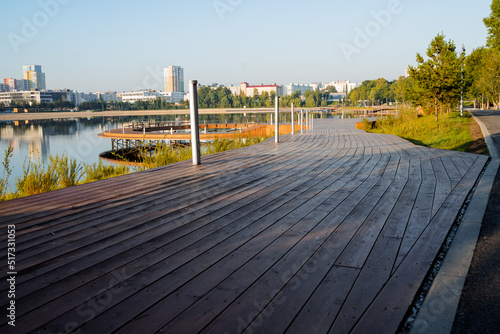 A road of boards, a wooden platform, a pedestrian path, a park in the city by the lake, a river embankment, a landscaped area, a place to relax.