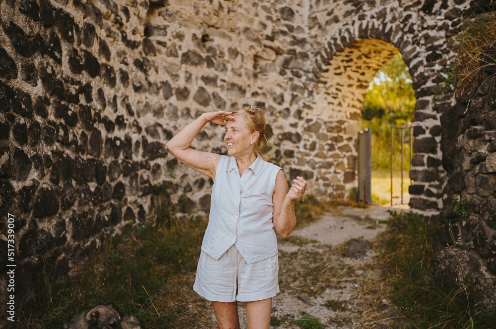 Elderly smiling senior traveling mature woman tourist walking posing outdoors in ancient Europe fortress. Retired people summer holiday vacation, active lifestyle concept